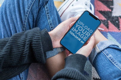 Mockup of a Woman with Crossed Legs Holding an iPhone 11 Pro