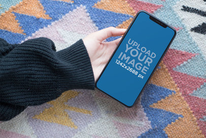 Mockup of a Woman's Hand Holding an iPhone 11 Pro Max Over a Carpet