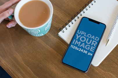 Mockup of an iPhone 11 Pro Over a Notebook on a Wooden Desk