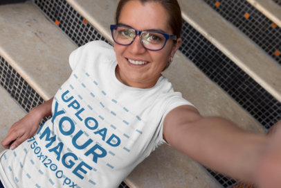 T-Shirt Mockup of a Happy Customer with Glasses Taking a Selfie on the Stairs