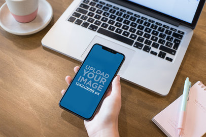Mockup of a Woman's Hand Holding an iPhone 11 Pro Max over a Wooden Desk