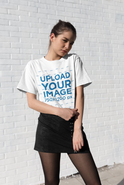 Tee Mockup Featuring a Cute Shy Woman Posing in Front of a Brick Wall 