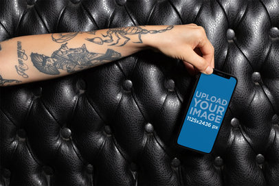 iPhone XS Mockup of a Tattooed Hand Over a Black Leather Sofa 25377