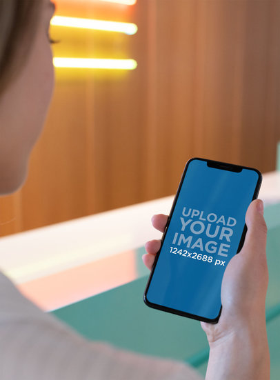 Mockup of a Girl Holding an iPhone XS Max in a Bright Corridor 25432