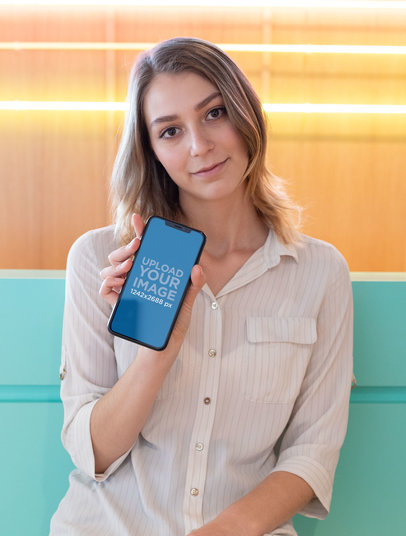 Mockup of a Cute Girl Holding Her iPhone XS Max in a Cool Illuminated Room 25433