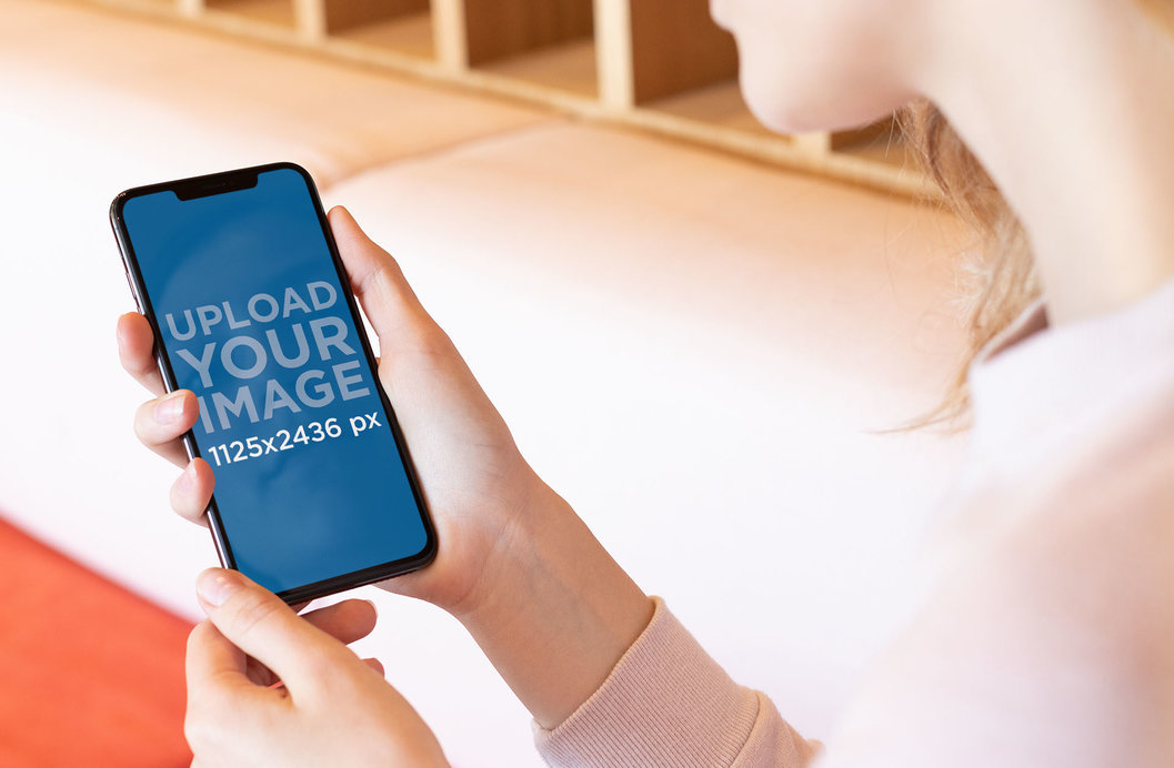 Over-The-Shoulder View Mockup of a Blonde Woman Looking at Her iPhone 11 Pro