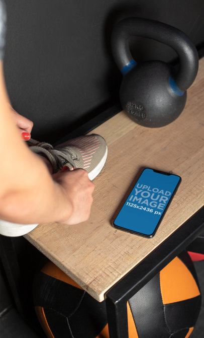Mockup of a Fitness Woman Tying Her Sneaker on a Bench Next to an iPhone 11 Pro Max
