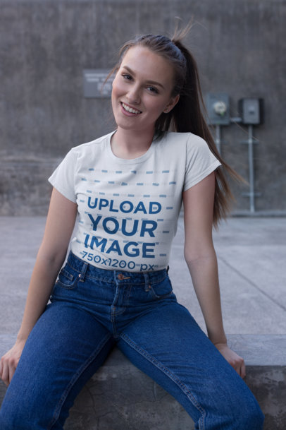 Tee Mockup Featuring a Woman Sitting on an Urban Concrete Surface