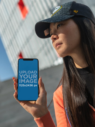 iPhone XS Mockup of a Long-Haired Girl with a Cap Staring into the Sky 25775