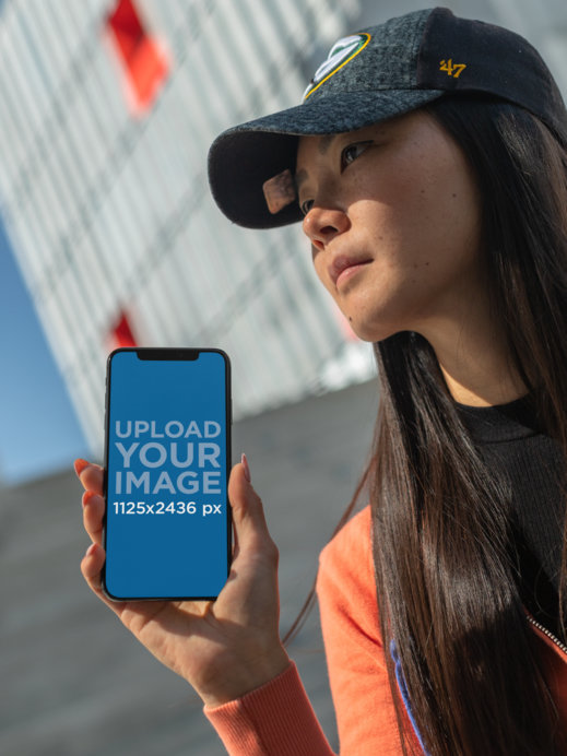 iPhone 11 Pro Mockup of a Long-Haired Woman with a Cap Staring into the Sky