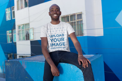 T-Shirt Mockup of a Smiling Man Sitting by an Apartment Complex
