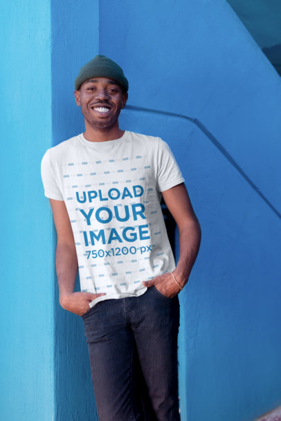 T-Shirt Mockup of a Smiling Man with a Beanie Casually Posing by a Blue Wall 26313