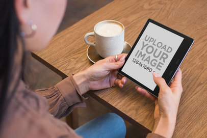 Mockup of a Woman Holding a Kindle Oasis While Sitting at a Cafe