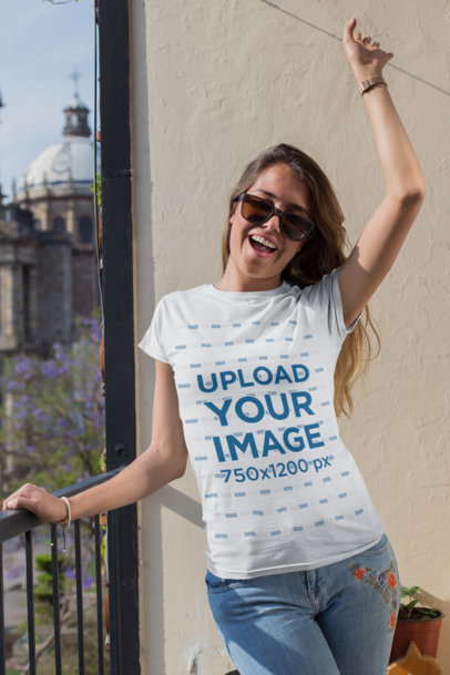 T-Shirt Mockup of a Cheerful Woman with Sunglasses Celebrating on a Balcony