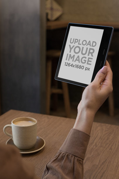 Mockup of a Woman Reading a Kindle Oasis by a Table with a Coffee Mug
