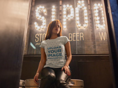 T-Shirt Mockup of a Seductive Girl Sitting in Front of a Bright Sign 18022