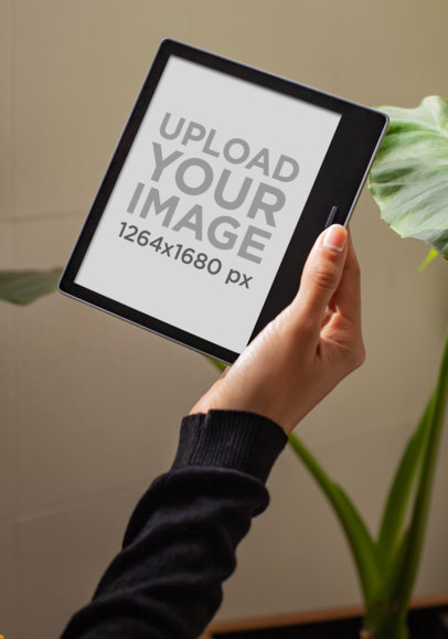 Mockup of a Woman's Hand Holding a Kindle Oasis by a House Plant