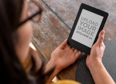 Mockup of a Woman Holding a Kindle Paperwhite on a Wooden Table
