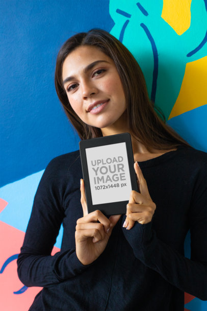Mockup of a Cute Woman Against a Colorful Wall Holding a Kindle Paperwhite 