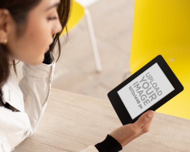 Mockup of a Woman on a Table Reading Her Kindle Paperwhite 