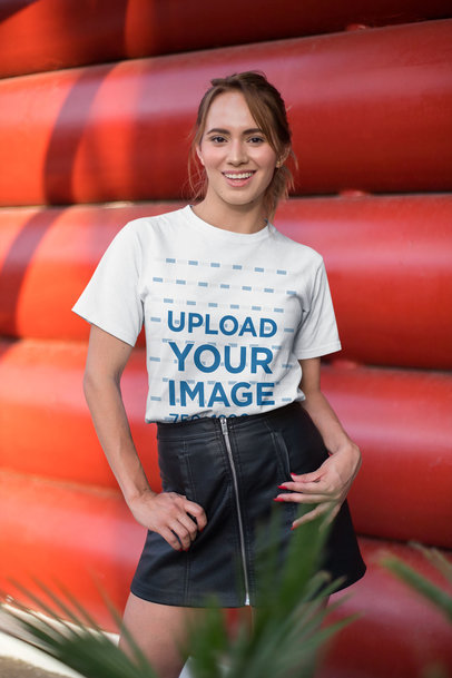 Tee Mockup of a Smiling Woman Standing in Front of a Red Structure