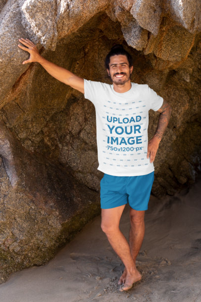 T-Shirt Mockup of a Tattooed Man Leaning Against a Big Rock by the Beach