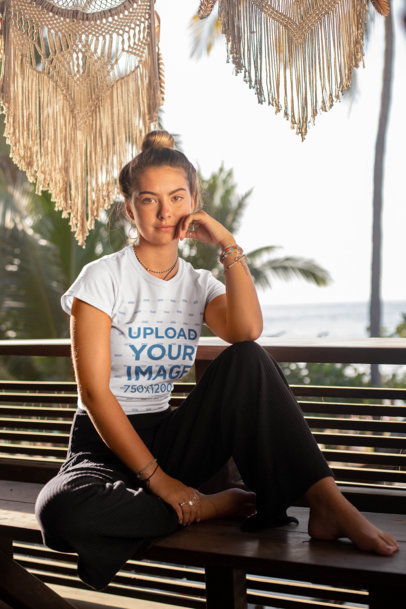 Tee Mockup of a Woman with a Hair Bun Sitting on a Bench by the Beach