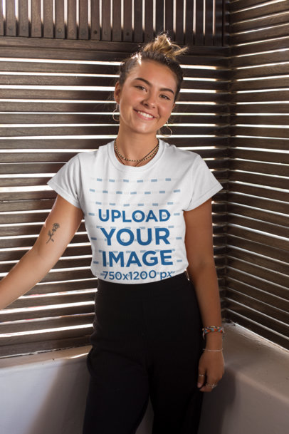 Tee Mockup of a Smiling Young Woman Against Wooden Blinds