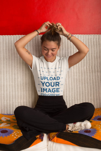 Tee Mockup of a Smiling Woman over a Wicker Couch Fixing Her Hair Bun