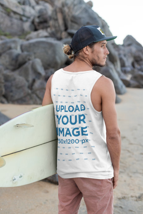 Back View Tank Top Mockup of a Young Man with a Cap Carrying a Surfboard by the Beach