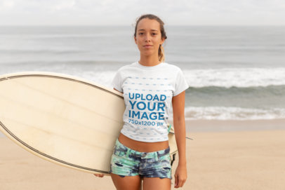 T-Shirt Mockup of a Young Woman with a Ponytail Carrying a Surfboard at the Beach
