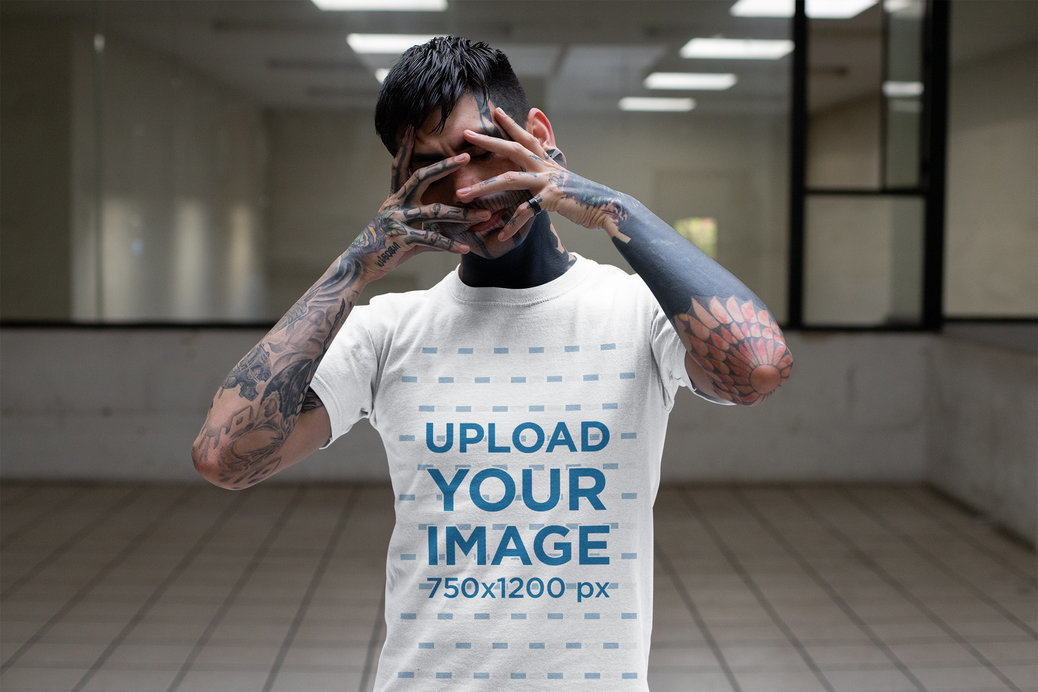 T-Shirt Mockup of a Tattooed Man Covering His Face in a Room