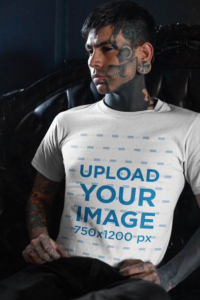 T-Shirt Mockup of a Goth Man with Tattoos All over His Body Sitting in a Dark Armchair