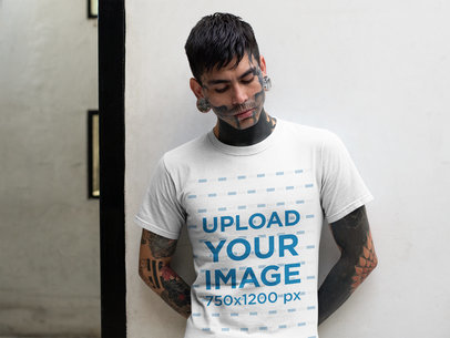 T-Shirt Mockup of a Tattooed Goth Man Leaning on a White Wall
