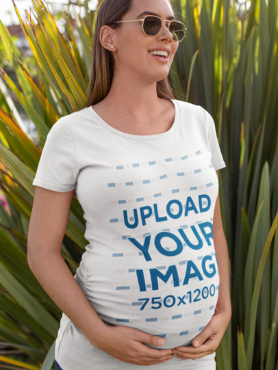 T-Shirt Mockup of a Pregnant Woman with Sunglasses Against Long Leaves