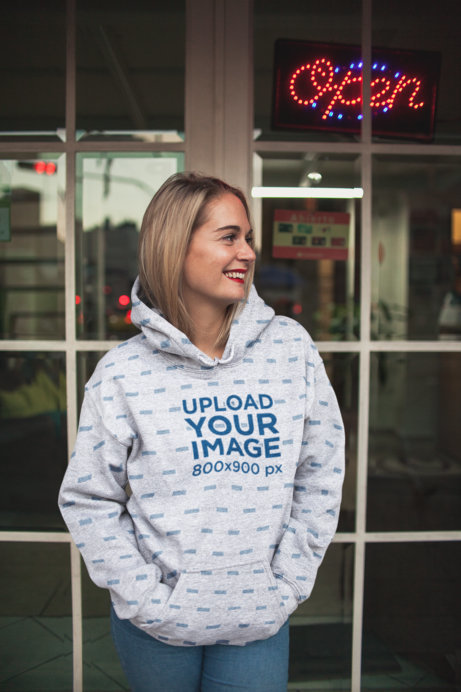 Hoodie Mockup of a Blonde Woman Standing Next to a Window Pane 