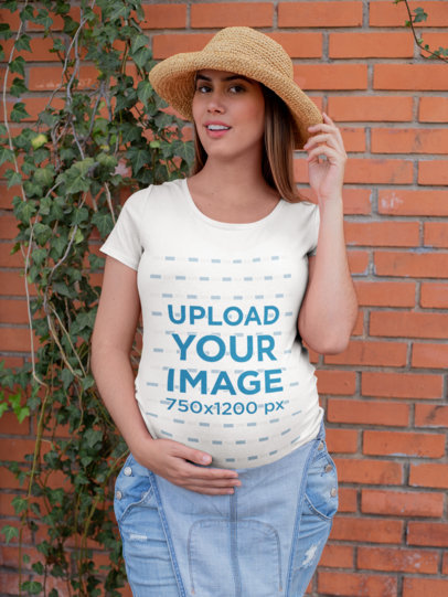 T-Shirt Mockup of a Pregnant Woman Posing in Front of a Brick Wall