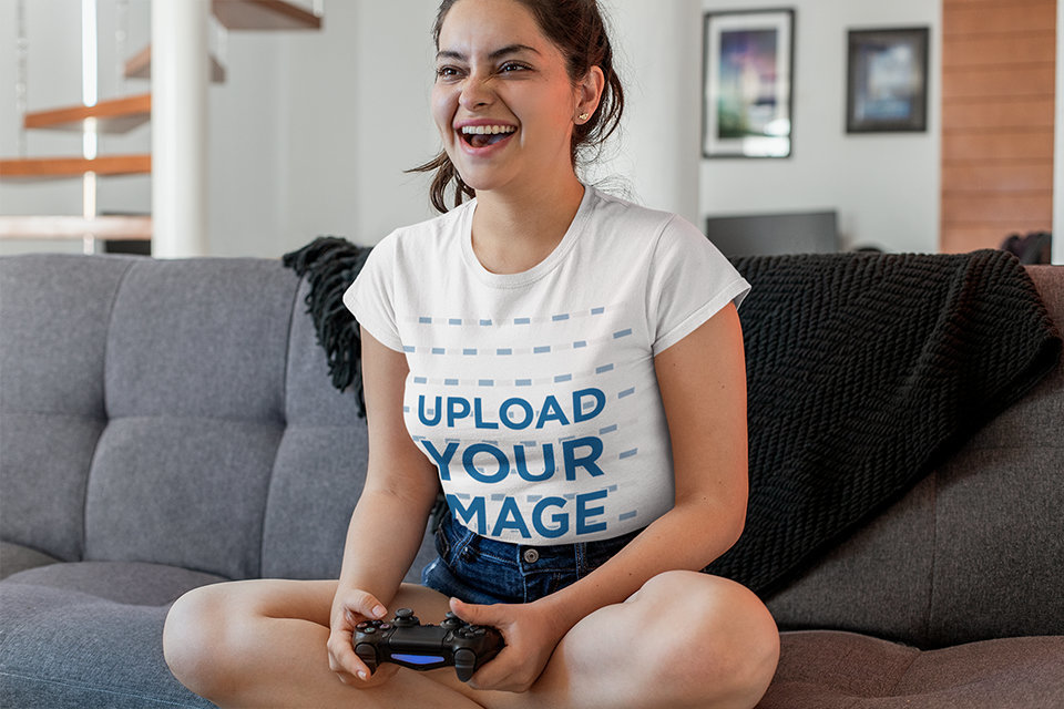 Tee Mockup Featuring a Joyful Woman on a Couch Playing Video Games