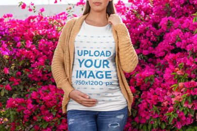 Mockup of a Pregnant Woman Wearing a T-Shirt in front of a Floral Bush