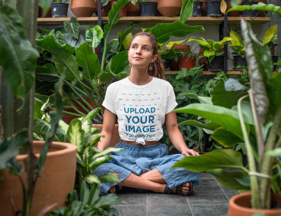 T-Shirt Mockup of a Relaxed Young Woman Sitting in a Greenhouse  