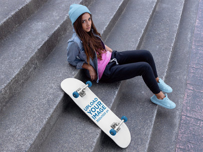 Skateboard Mockup of a Woman with a Beanie Sitting on a Concrete Stairway 