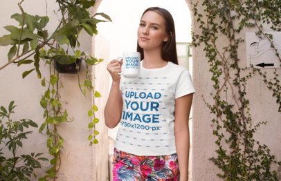 T-Shirt Mockup of a Woman Holding a 15 oz Mug Against a Wall Covered in Plants 27514