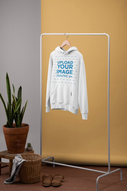 Women's Pullover Hoodie Mockup Hanging from a Simple Rack by a Plant Pot