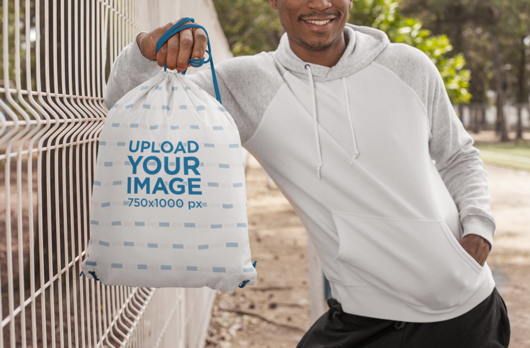 Drawstring Bag Mockup Featuring a Man Leaning Against a Wire Fence