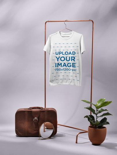 T-Shirt Mockup Hanging From a Rack Next to a Vintage Suitcase and a Plant