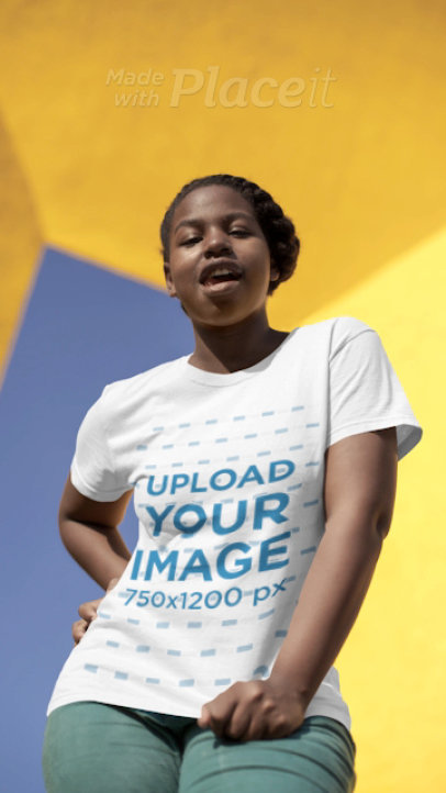 T-Shirt Video Featuring a Joyful Woman Posing in Front of a Yellow Concrete Structure 