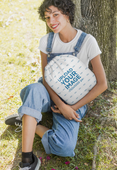 Mockup Featuring a Woman Holding a Drawstring Bag Sitting Under a Tree 27598
