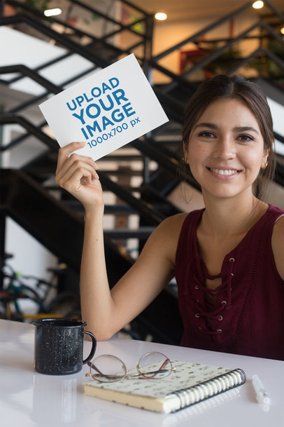 Mockup of a Smiling Woman at a Table Holding an A5 Flyer