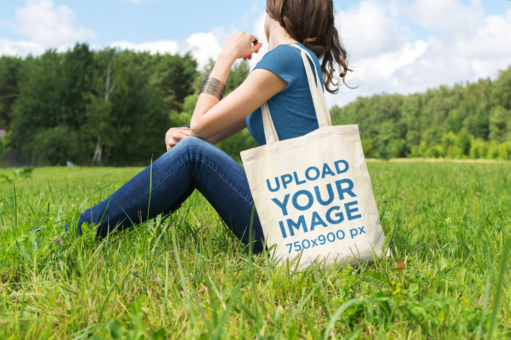 Tote Bag Mockup of a Woman Sitting at a Green Meadow