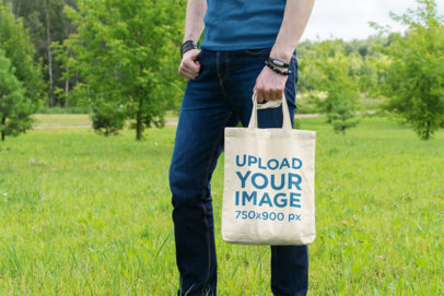 Mockup of a Man Holding a Tote Bag in an Open Field 25-el